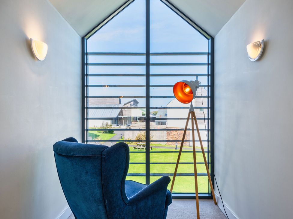 A seating area with a blue armchair and floor lamp at Chapel Park Marhamchurch