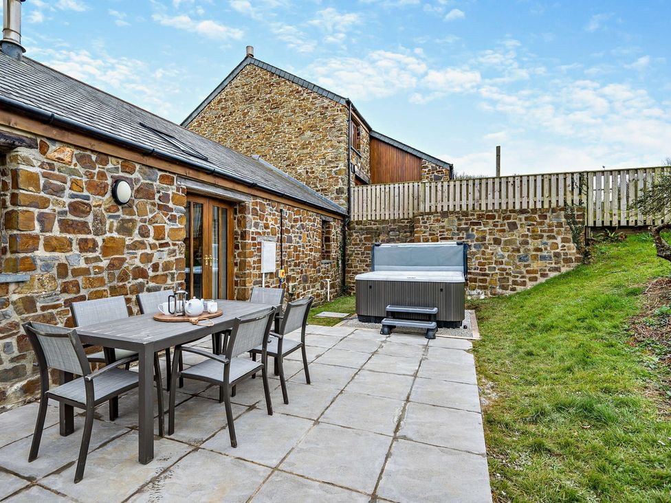 An outdoor patio with a table and chairs next to a hot tub at Long Down Spa in Marhamchurch