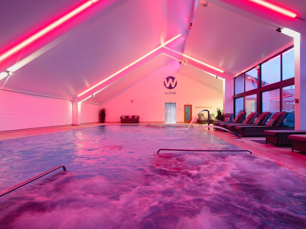An indoor pool area with lounge chairs and water features at Long Down Spa in Marhamchurch