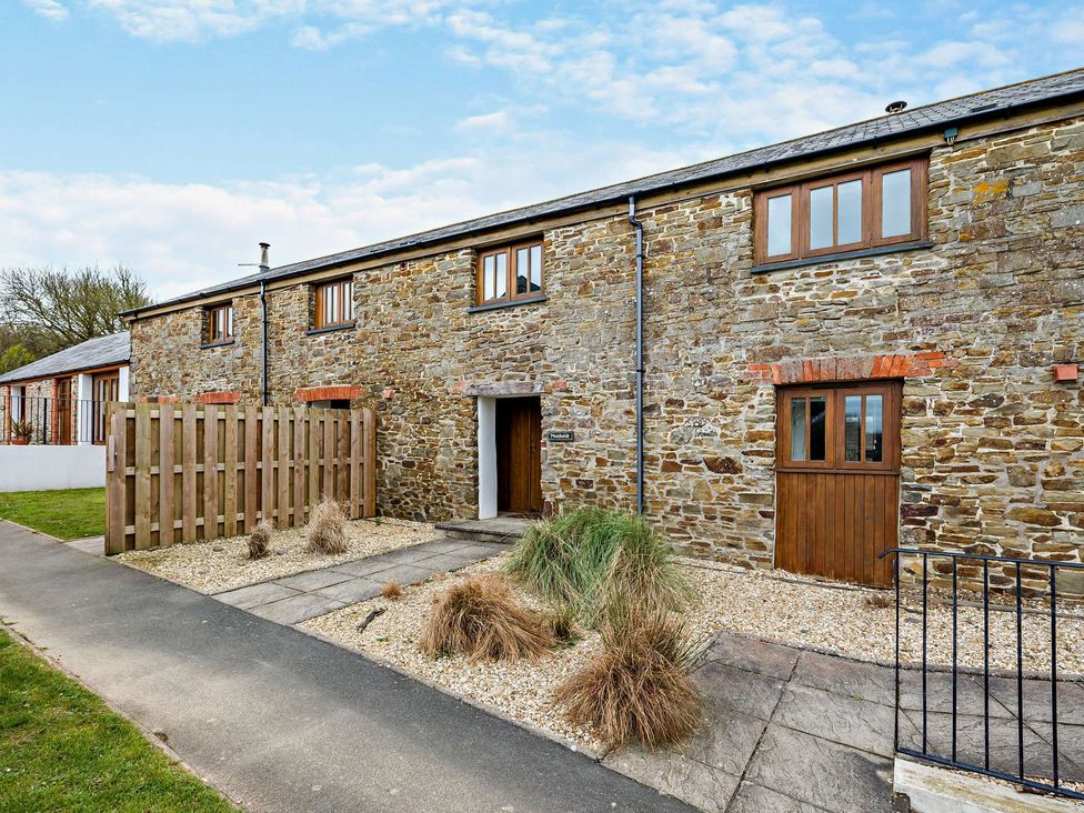 An outdoor view of a stone building with wooden fence at Middle Hill in Marhamchurch