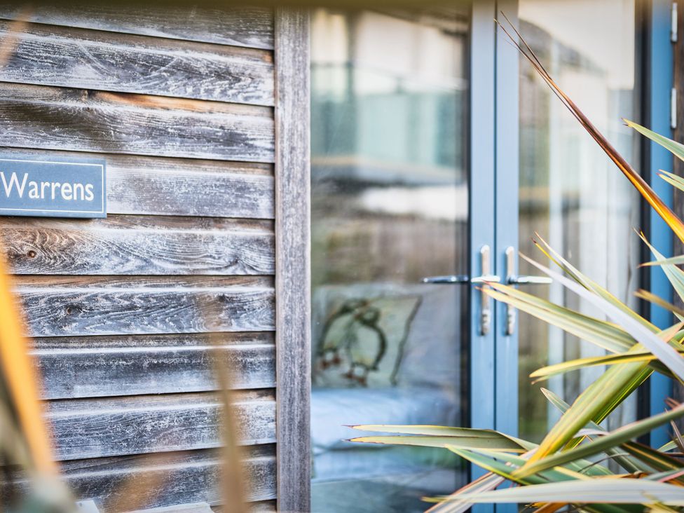 A wooden wall with a sign and glass door at Warrens Spa in Marhamchurch