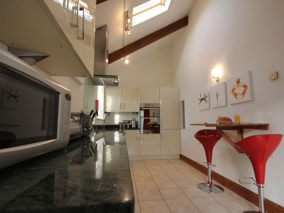 A kitchen with a microwave, cabinets, bar stools, and countertop at Westcotts in Marhamchurch