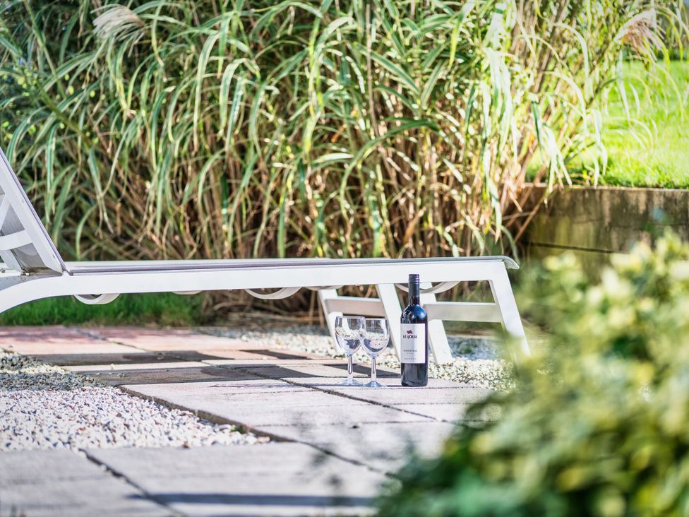 A lounge chair with a wine bottle and glasses on a patio at Arundell Marhamchurch
