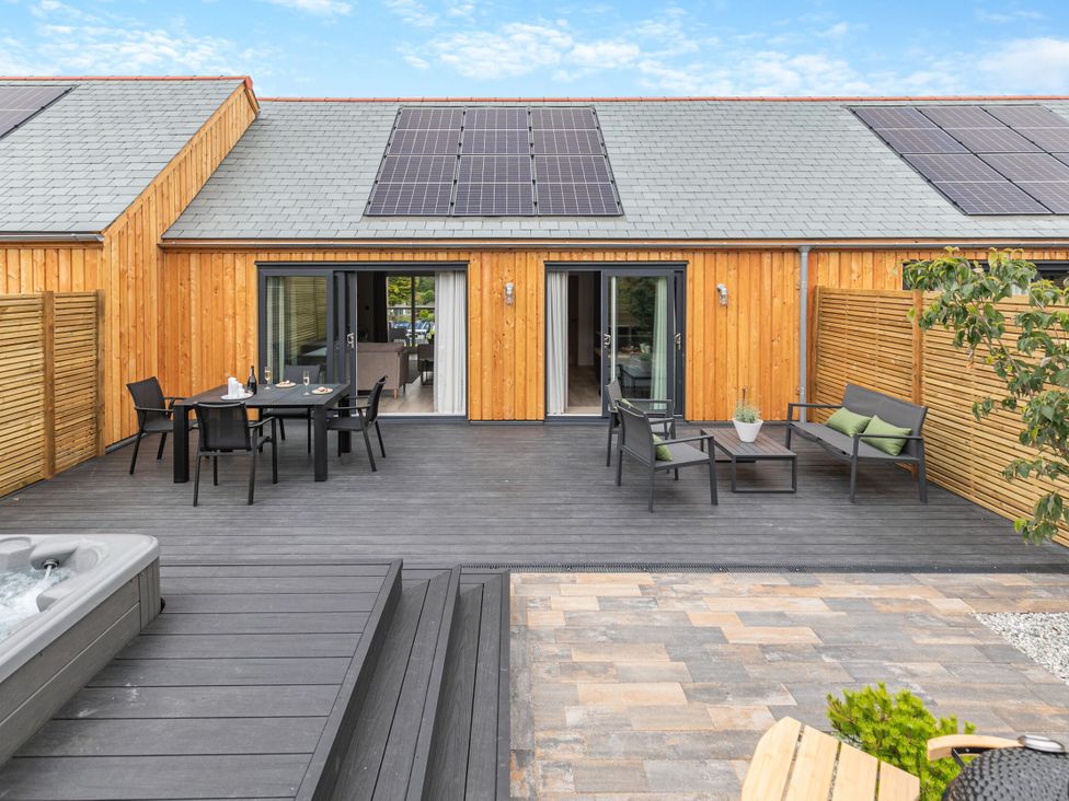 An outdoor area with decking, a table, chairs, and a spa at Gwari Spa Barn 3.0 in Marhamchurch