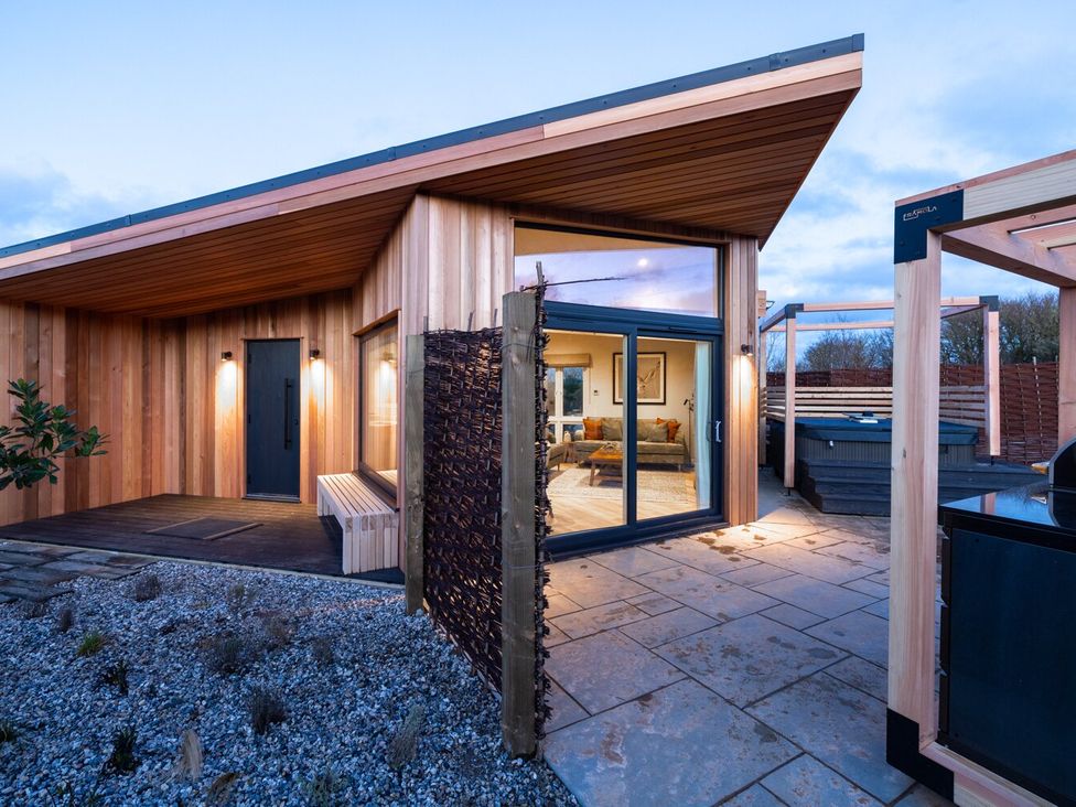 An exterior view of a modern wooden house with a hot tub at Trelowen 3.0 Spa in Marhamchurch