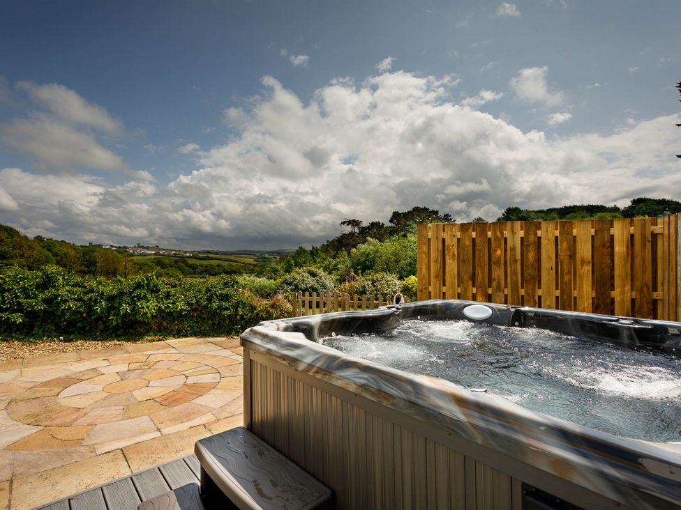 An outdoor area with a hot tub and patio at Whalesborough Cottage Spa in Marhamchurch