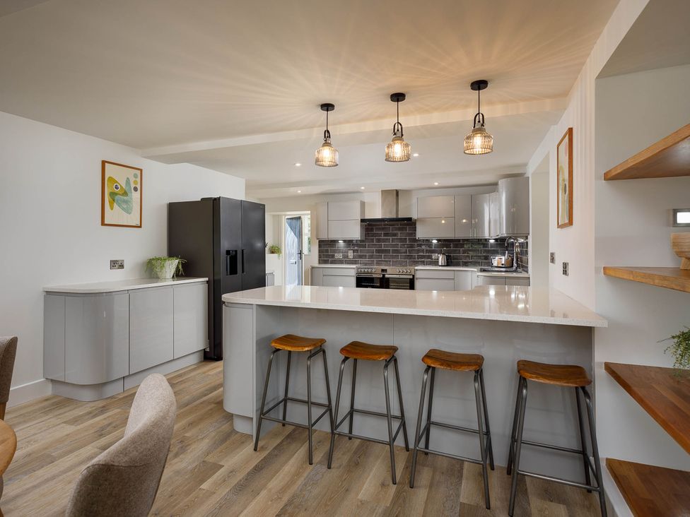 A kitchen with an island counter and bar stools at Whalesborough Cottage Spa Marhamchurch