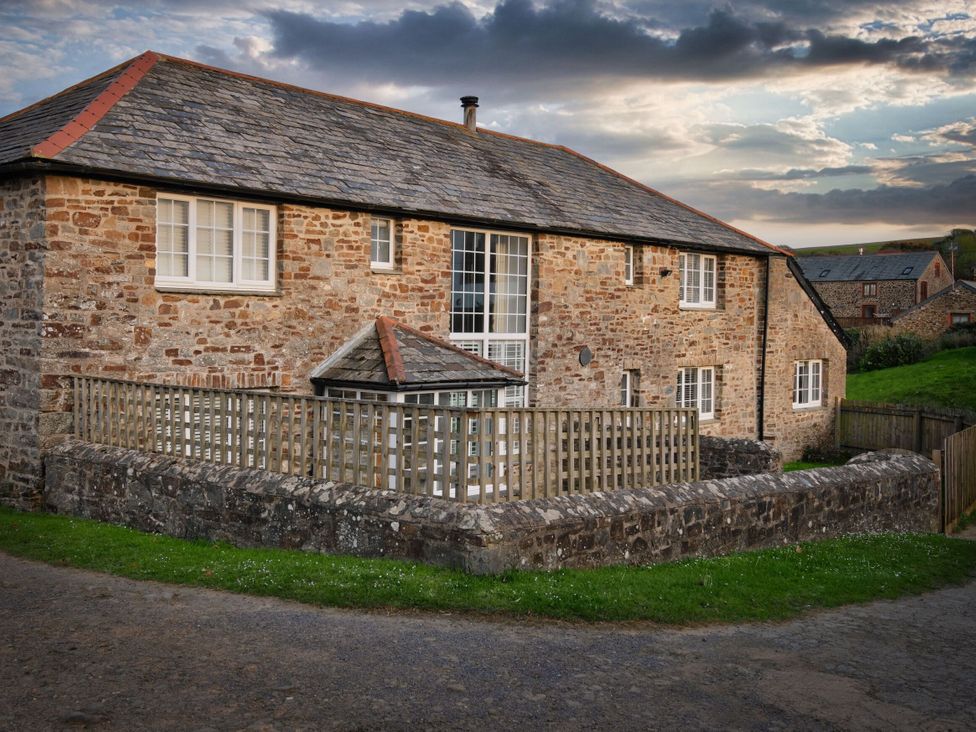 A stone building with windows and a wooden fence at Calf House Spa in Marhamchurch