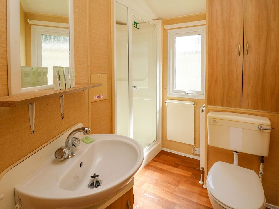 A bathroom with a sink, toilet, shower, and mirror at Caravan 2 at Blackmoor Farm near tenby