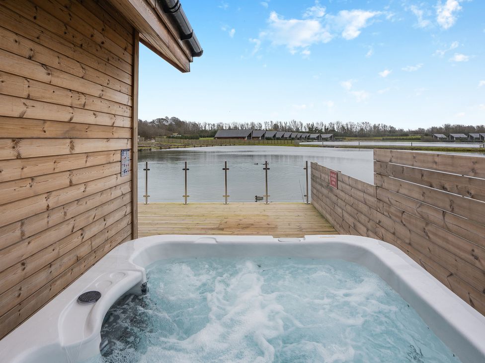 A hot tub on a wooden deck facing a body of water at Tranquillity 4 in Carnforth