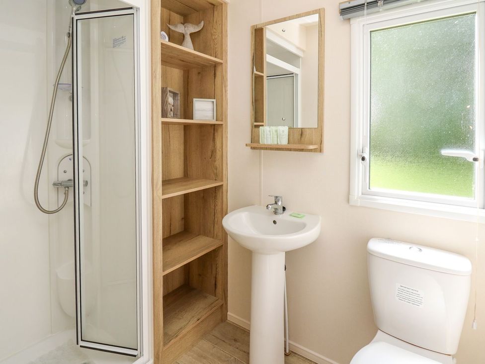A bathroom with a shower unit and storage shelf at Caravan 6 at Blackmoor Farm near tenby Narberth