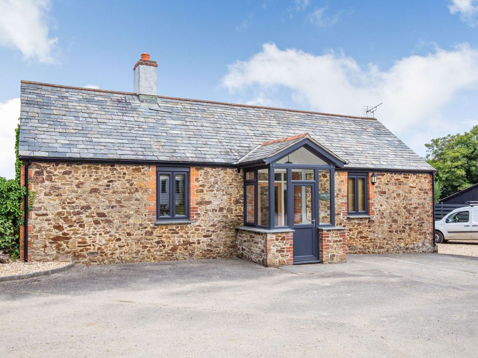 The exterior of a stone cottage with a parking area at Godolphin Stable Bude