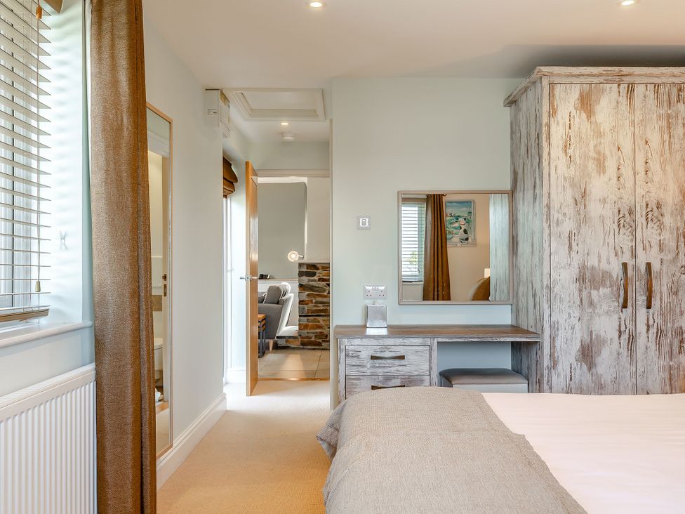 A bedroom with a bed, wardrobe, and mirror at Godolphin Stable in Bude