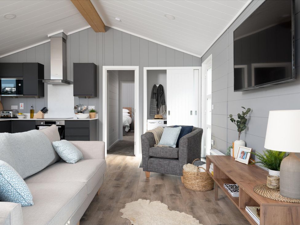 A living room with a sofa, armchair, and television at Kynance Spa Bude