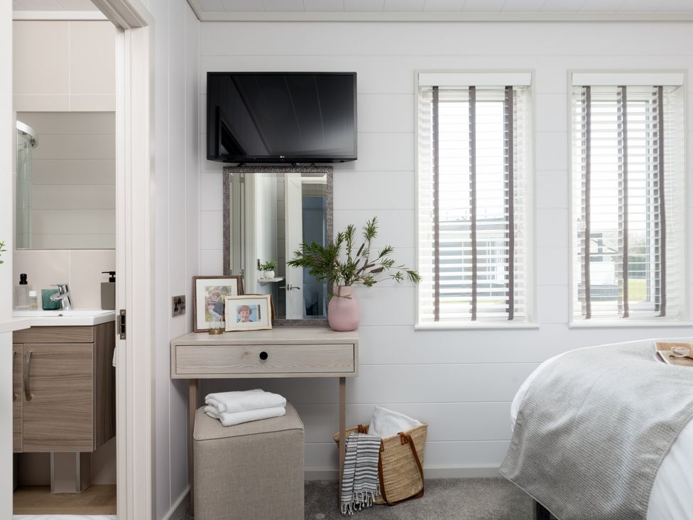 A bedroom with a television, console table, and windows at Sennen 3 Spa Roof Terrace (Pet) Bude