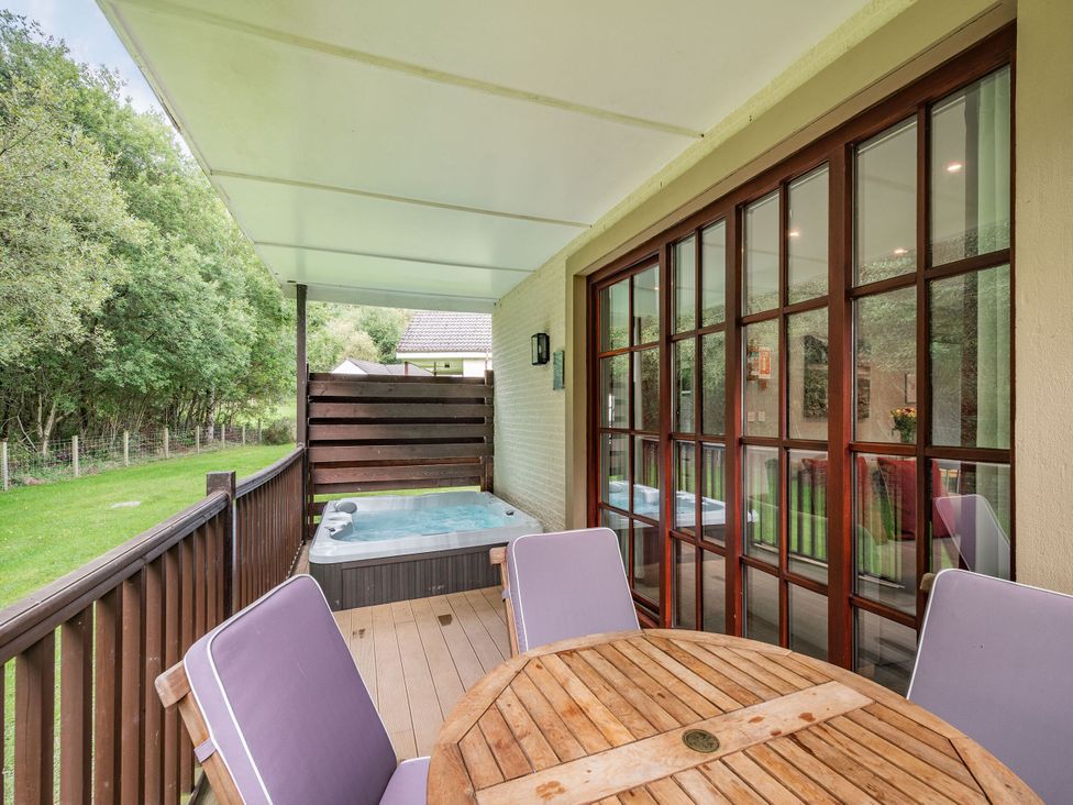 An outdoor patio with a hot tub and table at Arran Lodge Spa in Dailly