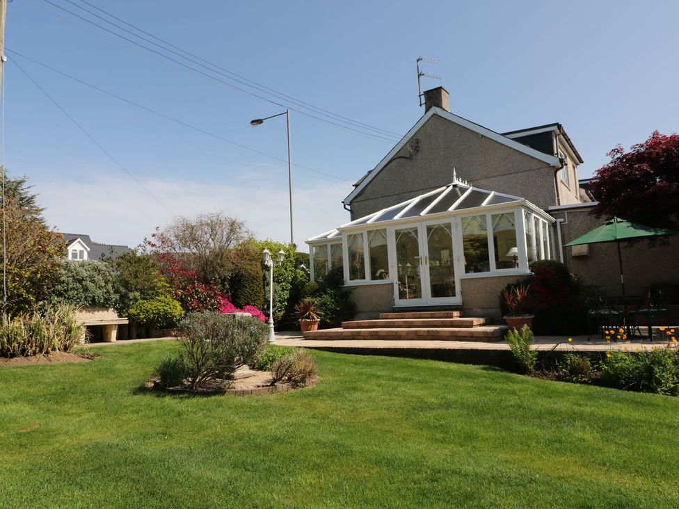 A garden with a conservatory and patio area at Llwyn Derw in Talybont