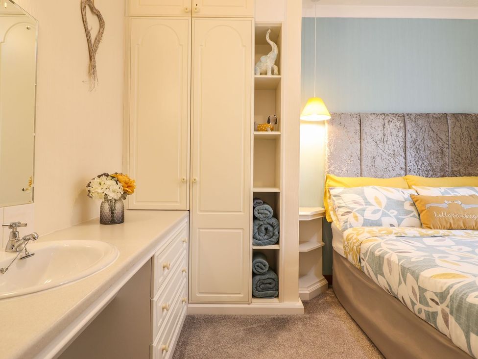 A bedroom with a bed, wardrobe, mirror, and sink at Llwyn Derw in Talybont