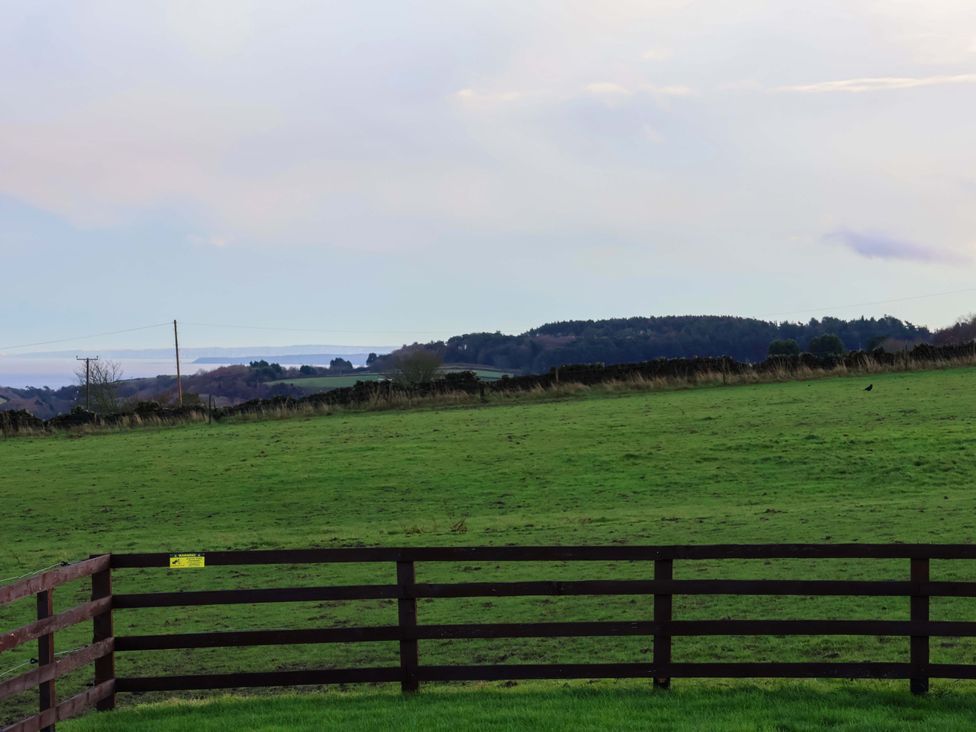 A field with a wooden fence and distant hills at Rosefinch Cabin in Scarborough