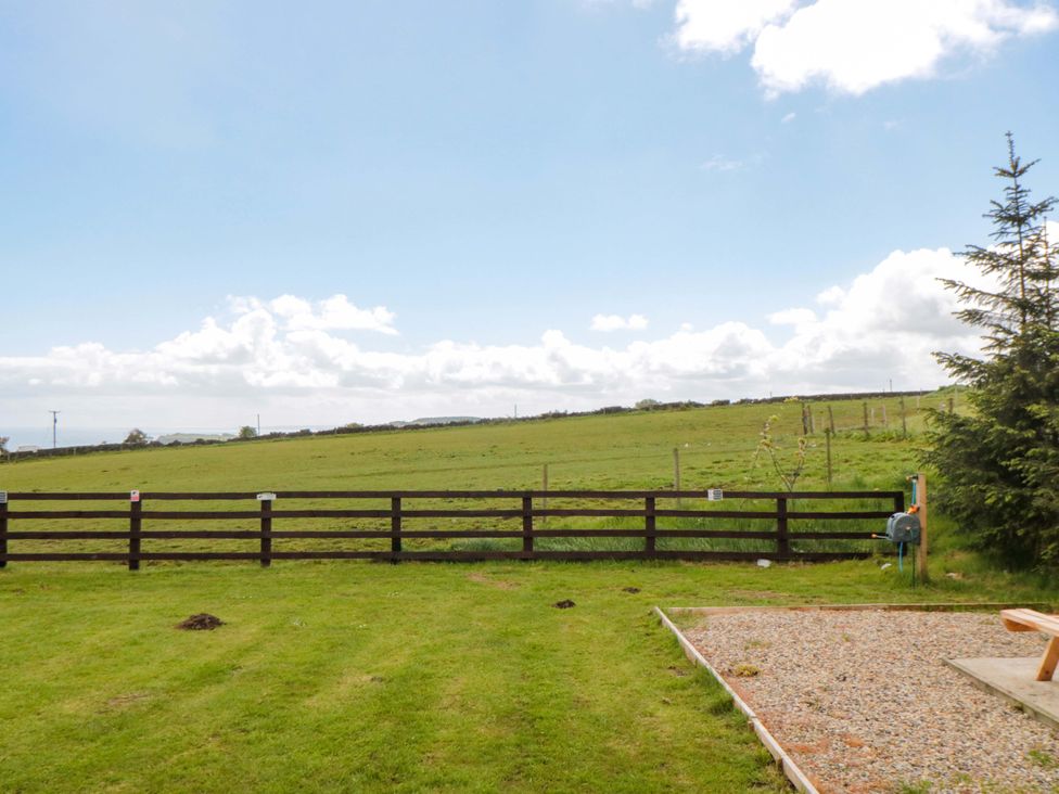 A grassy area with a fence and trees at Swift Cabin in Staintondale near Scarborough