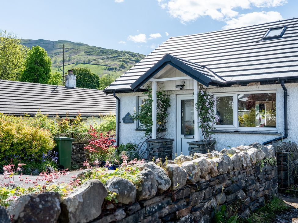 A cottage with a stone wall and flowers outside at Oaks Lodge Cottage Ambleside