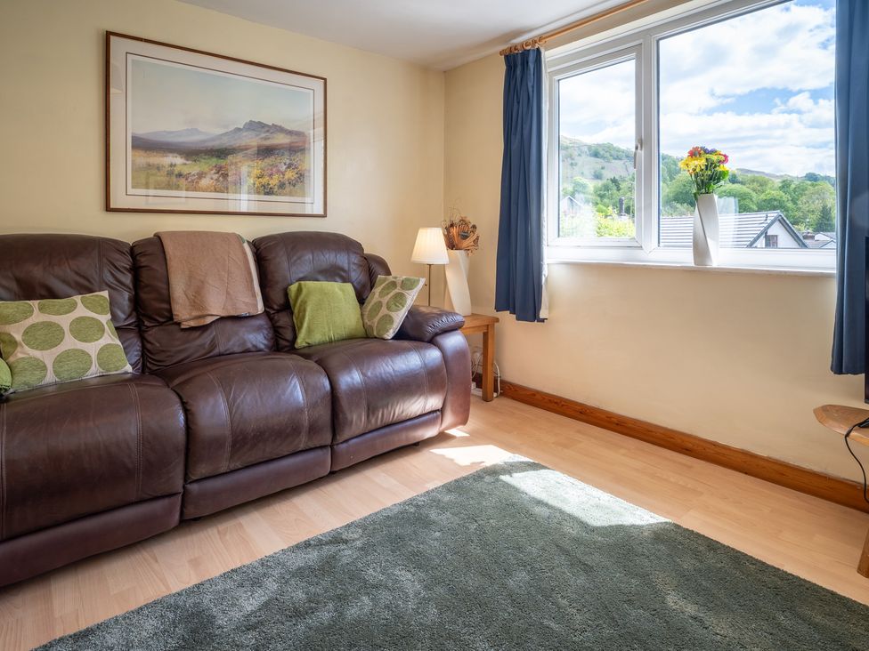 A living room with a sofa, cushions, lamp, and window at Oaks Lodge Cottage in Ambleside