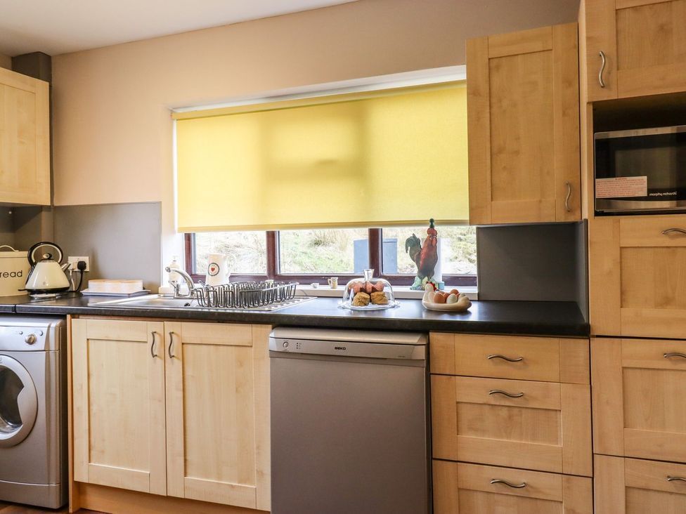 A kitchen with wooden cabinets, sink, washing machine, and a window at Baywood Cottage Keighley