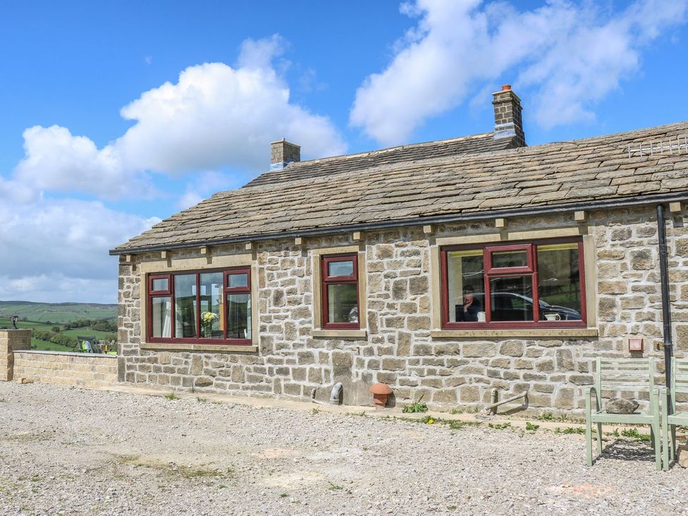 An exterior view of a stone house with windows and a chimney at Baywood Cottage in Keighley
