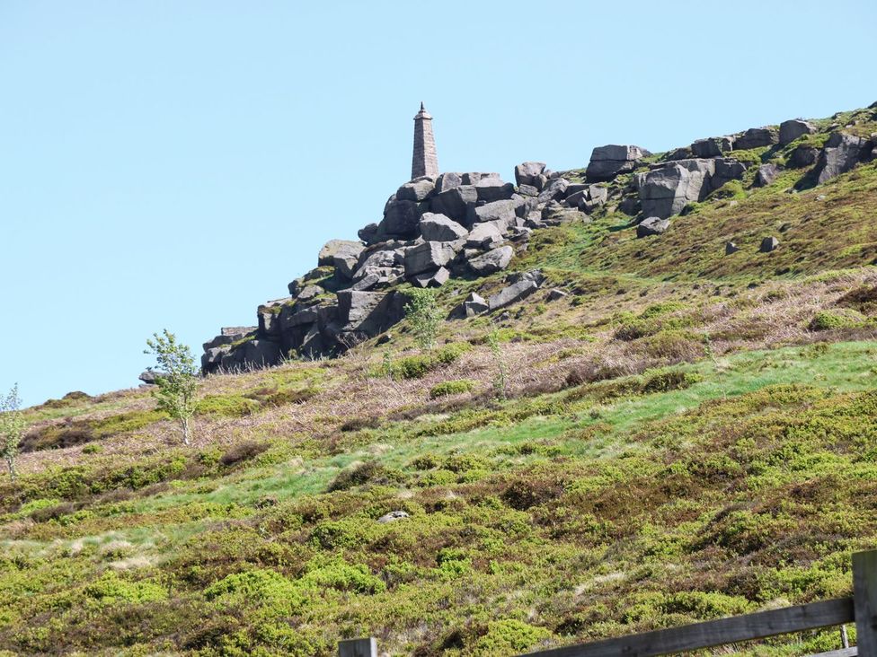 A rock formation with a tall stone monument on a hill at Baywood Cottage in Keighley