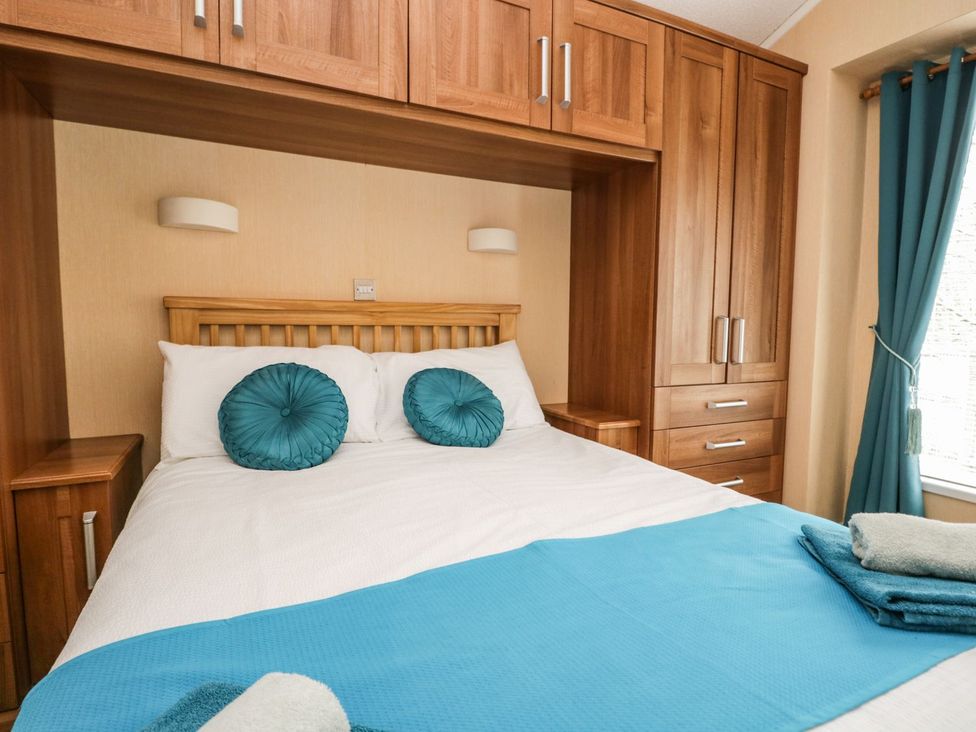 A bed with teal pillows and wooden furniture at Kingfisher Lodge Windermere