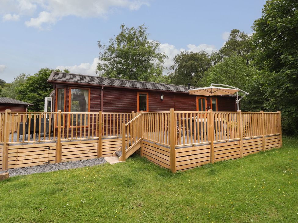 A cabin with a wooden deck and parasol at Kingfisher Lodge in Windermere