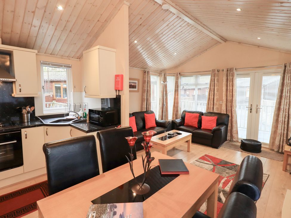 A living room with kitchen area and dining table at Kingfisher Lodge Grasmere 33, White Cross Bay near Windermere