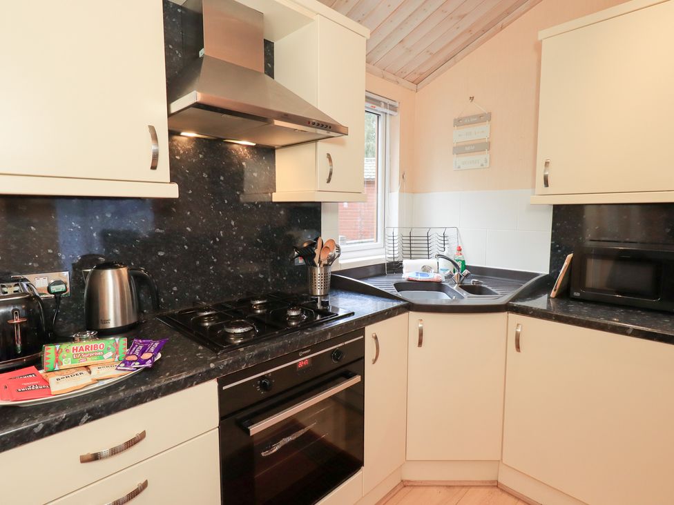 A kitchen with a kettle, cooker, sink, and microwave at Kingfisher Lodge Grasmere 33, White Cross Bay near Windermere