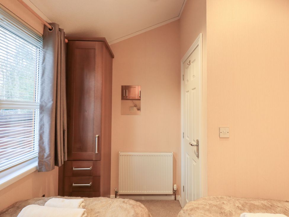 A bedroom with a wardrobe and window at Kingfisher Lodge, Grasmere 33, White Cross Bay near Windermere
