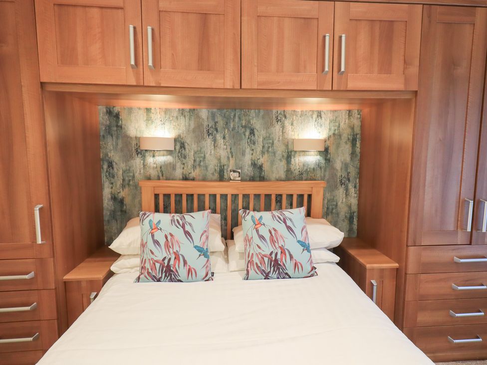 A bedroom with a bed and wooden cabinetry at Kingfisher Lodge Grasmere 33, White Cross Bay near Windermere