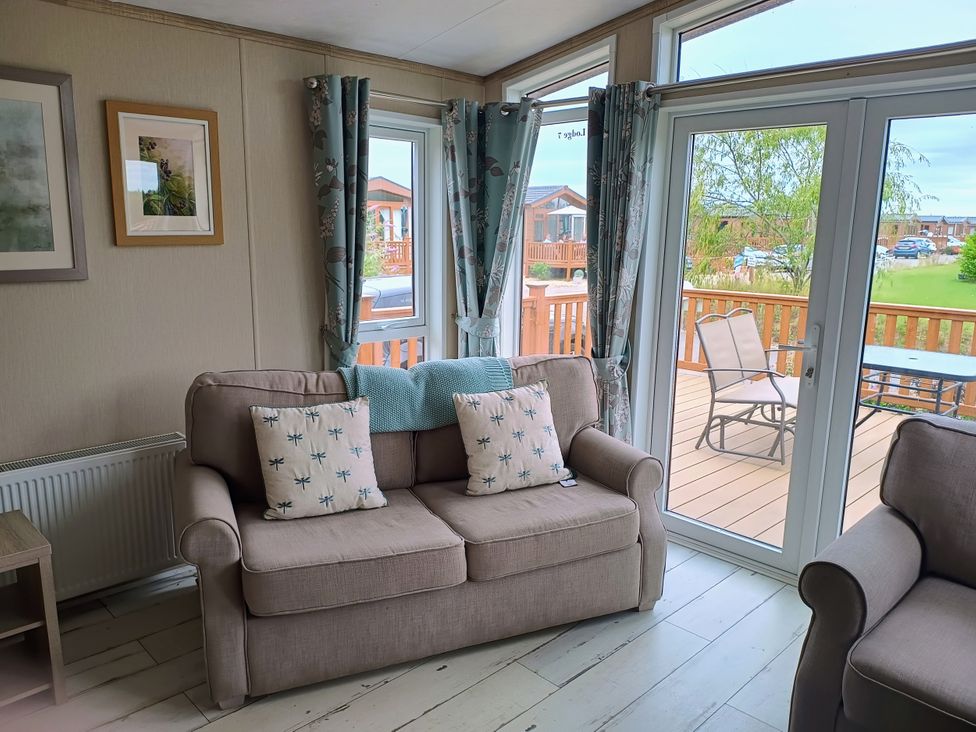 A seating area with a sofa and door leading to deck at Fern Lodge in Stowmarket