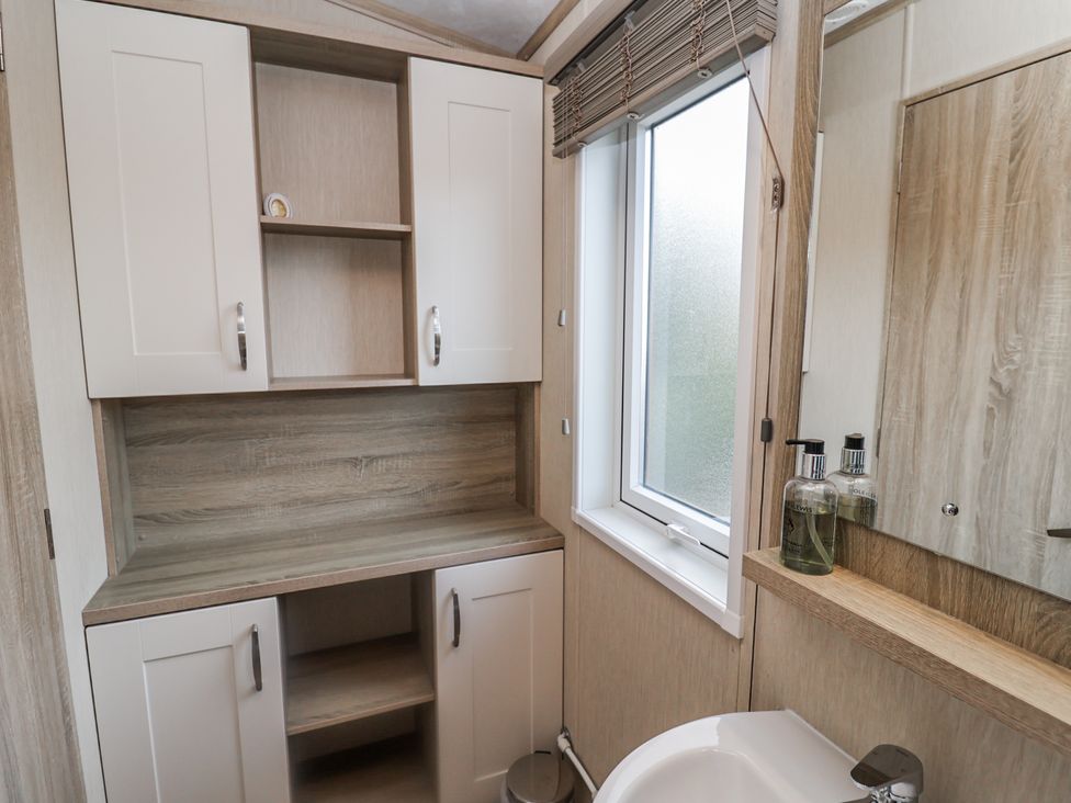 A bathroom with a sink, cabinet, and mirror at Fern Lodge in Stonham Aspal