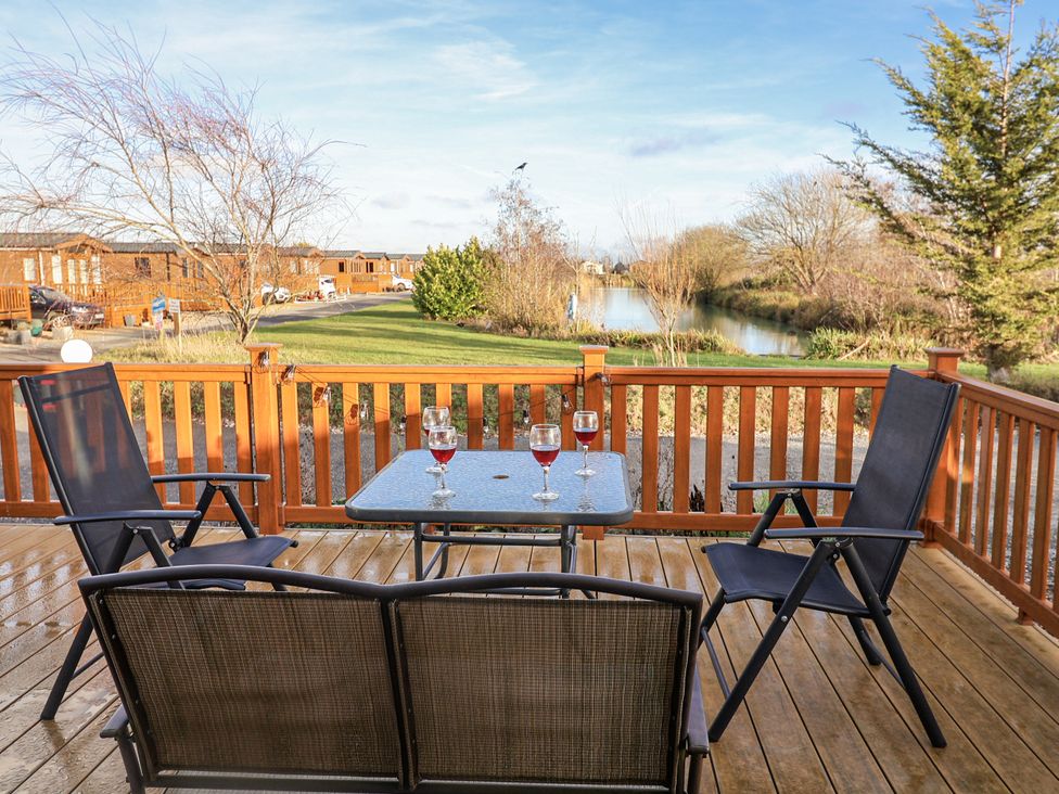 A terrace with a table and chairs overlooking a pond at Fern Lodge in Stonham Aspal