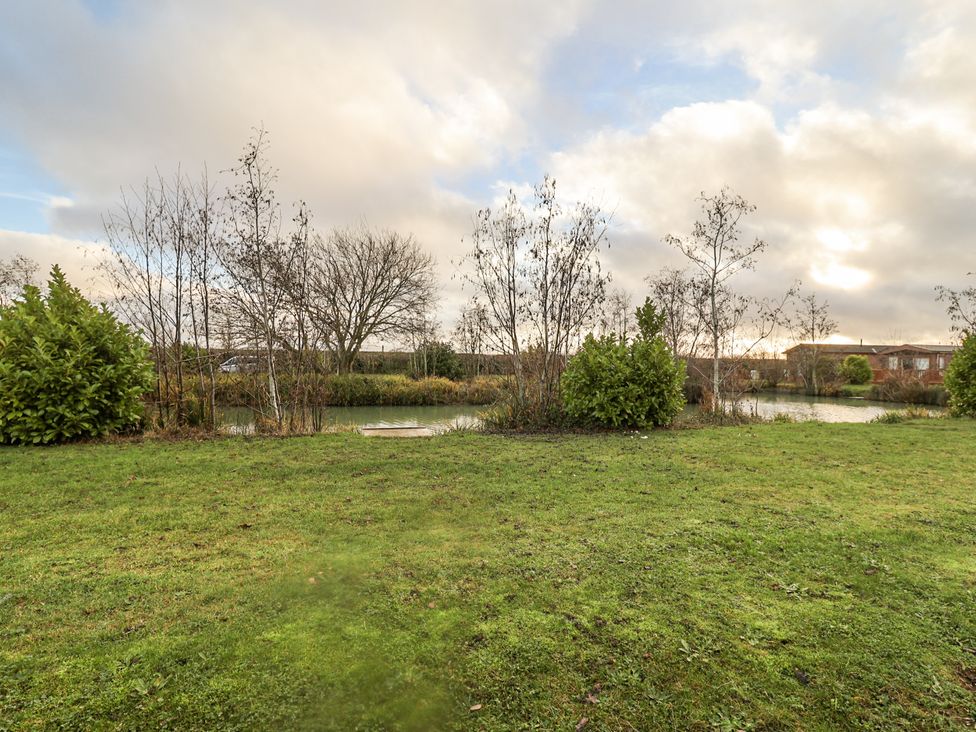 A garden with grass and trees near a pond at Fern Lodge in Stonham Aspal