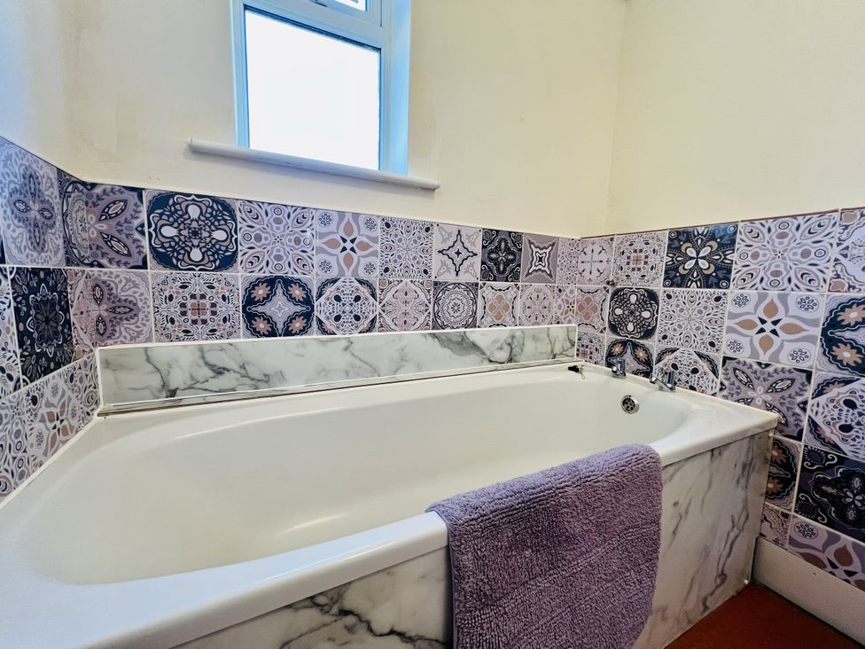 A bathtub with a towel and patterned tiles at 11 Langer Road in Felixstowe