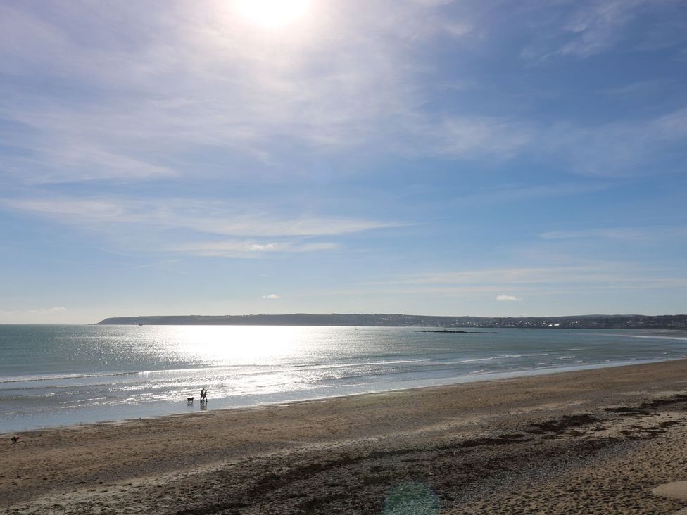 A beach with people walking on the sand and water in the background at Praa Waves in Penzance