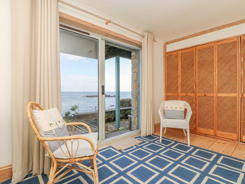 A living room with rattan and white chairs and a sliding door at Harbour Lights in Penzance