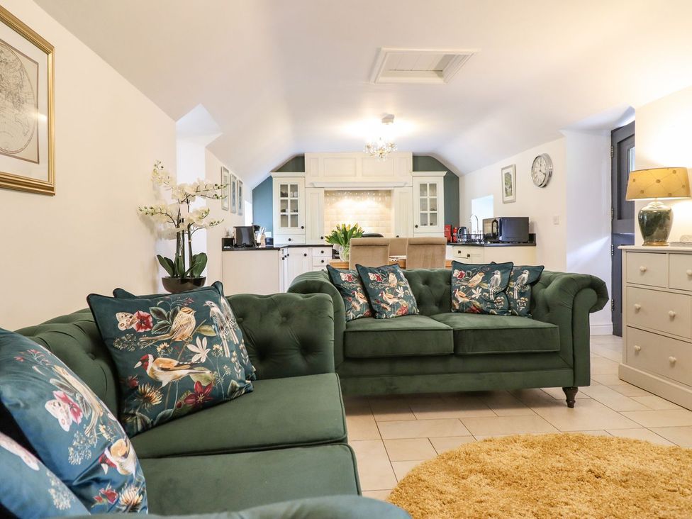 A living room with a green sofa and kitchen in view at The Talkhouse Cottage Caersws