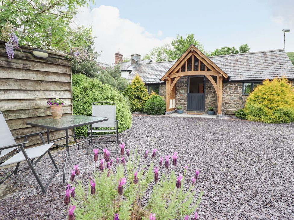 A garden with a table, chairs and flowers at The Talkhouse Cottage in Caersws