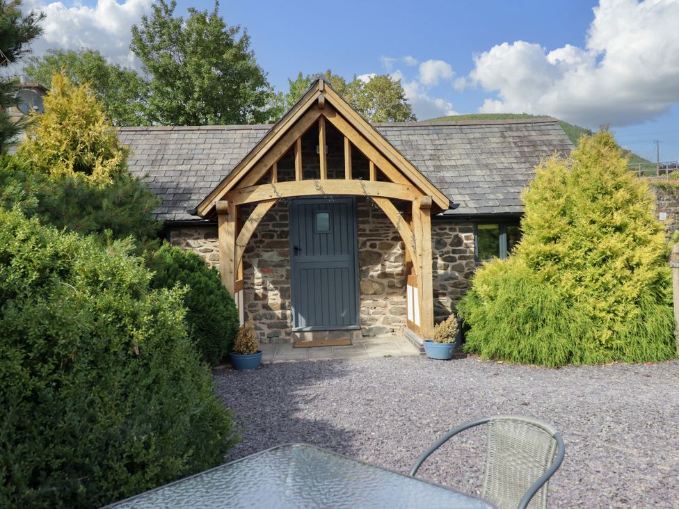 An exterior view of a stone building with a wooden porch at The Talkhouse Cottage in Caersws