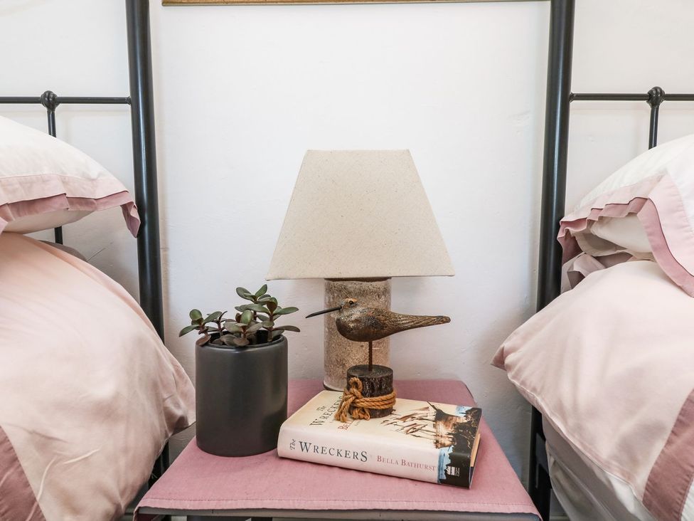 A bedside table with a lamp and a book at Driftwood Cottage in Helston