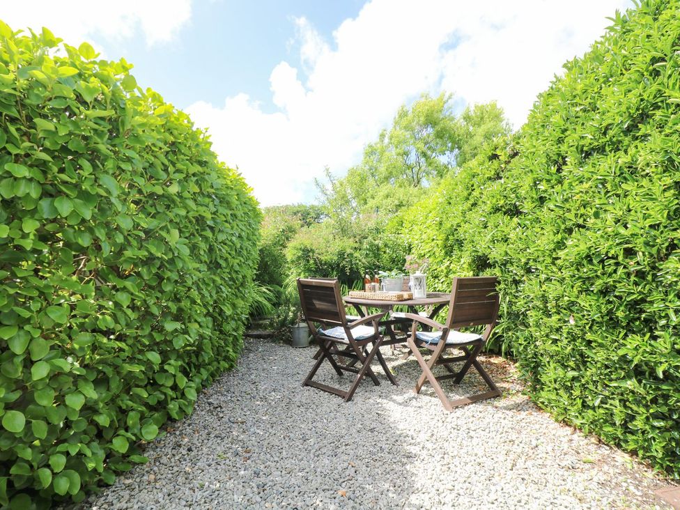 A garden with a table and chairs surrounded by hedges at Driftwood Cottage in Helston