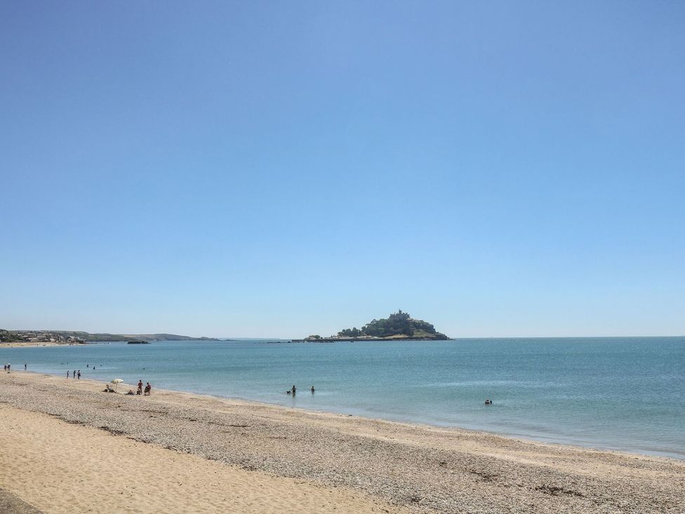 A beach with people swimming and an island visible at Driftwood Cottage Helston
