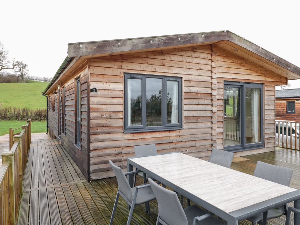 A wooden cabin with a deck and table and chairs at Birch Lodge in Rugeley