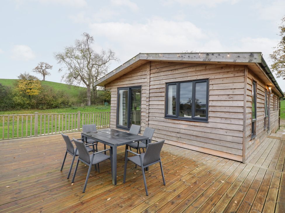 An outdoor area with a wooden lodge and table with chairs at Cedar Lodge in Rugeley